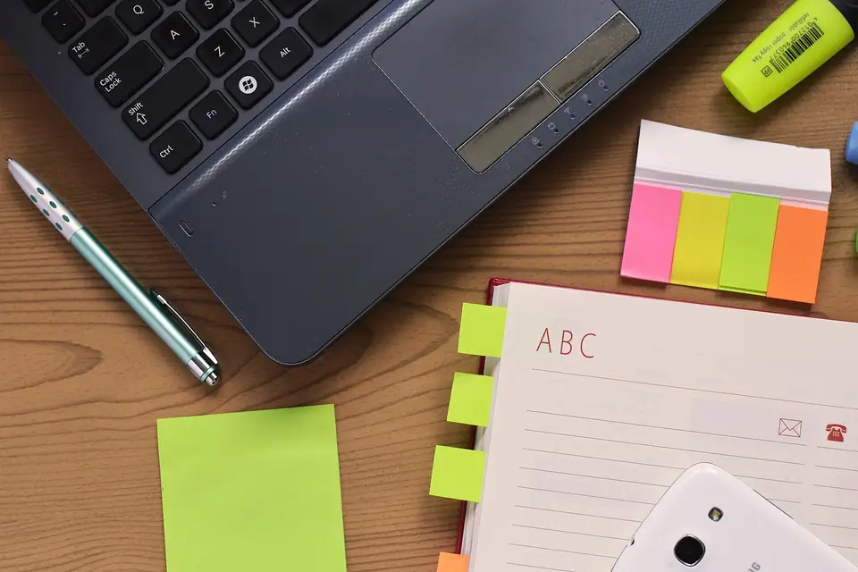 Yukarıdan görülen masada dizüstü bilgisayar, kalem, defter ve yapışkan notlar