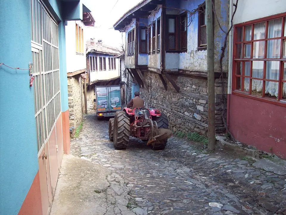 Taş döşeli köy sokağında tarihi evlerin önünde duran kırmızı bir traktör